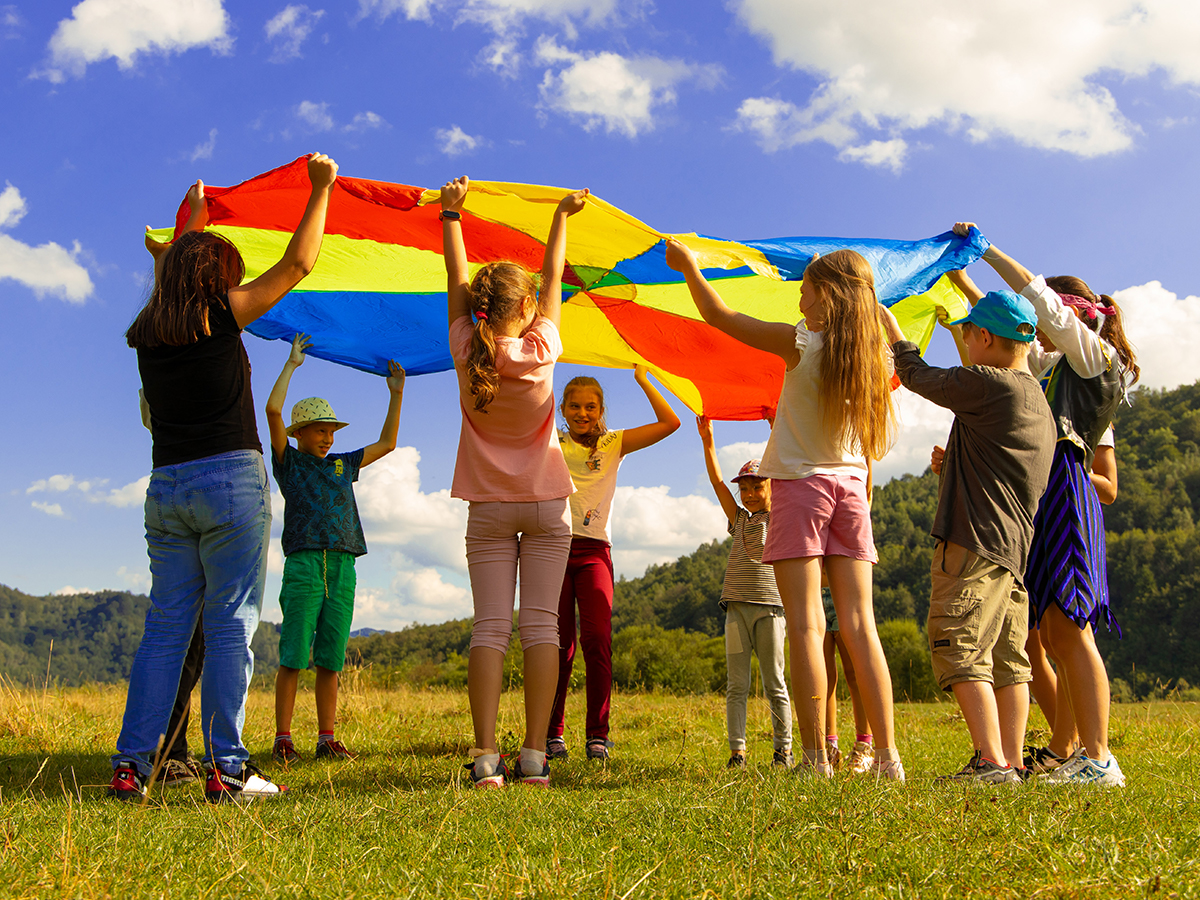 Kids playing with a rainbow tarp in an open field