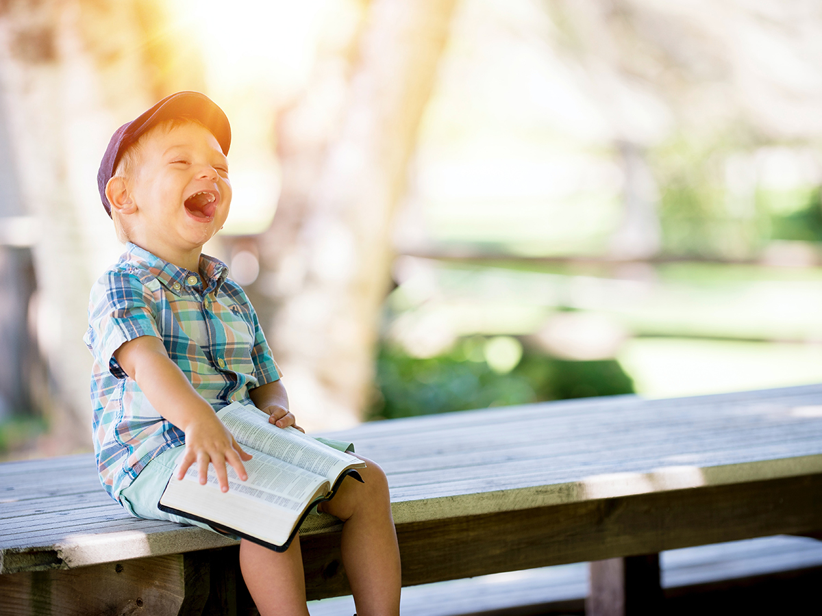 Child in nice clothes sitting on a bench with a book while laughing