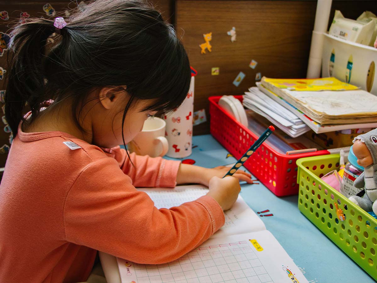 A young girl writing in a notebook at a desk