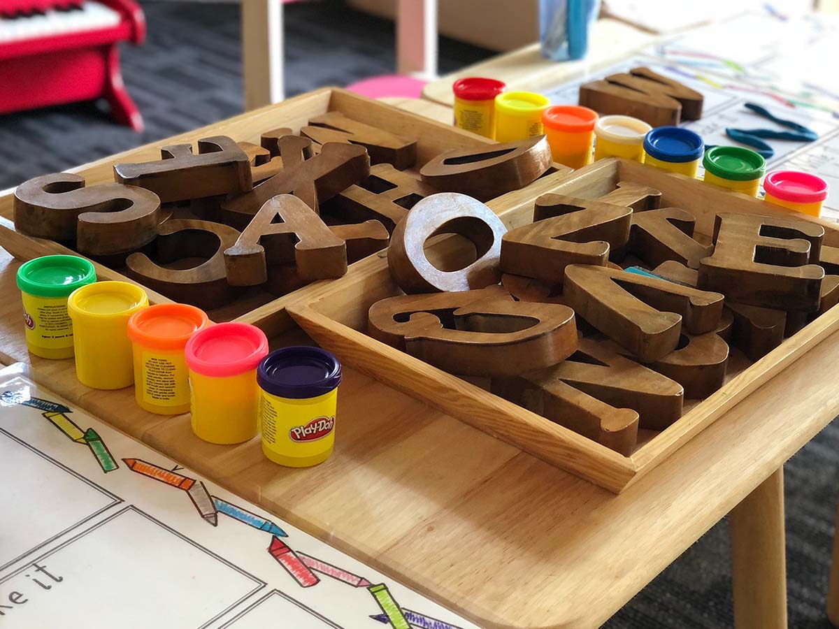 A child's desk with playdoh, wooden letter, and other toys