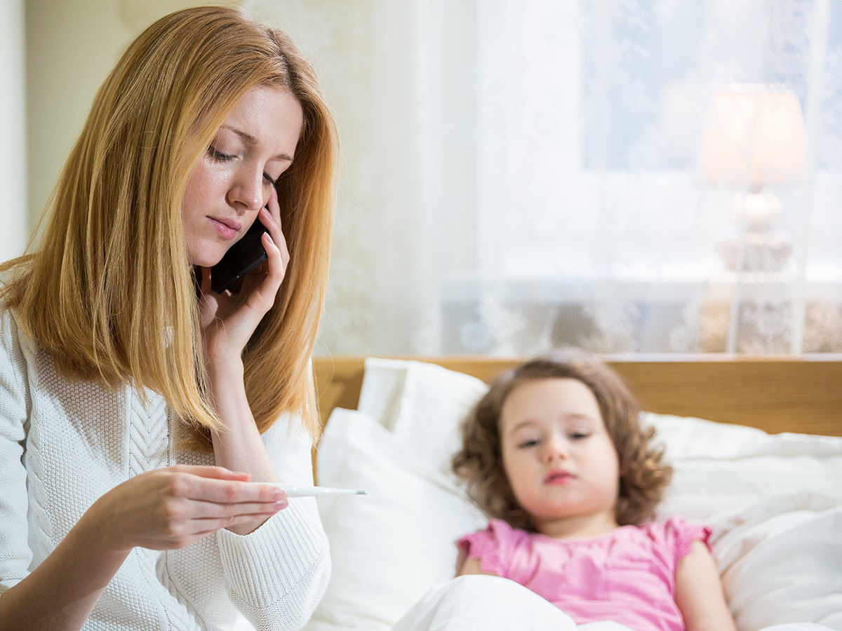 mother holding thermometer with sick child in bed