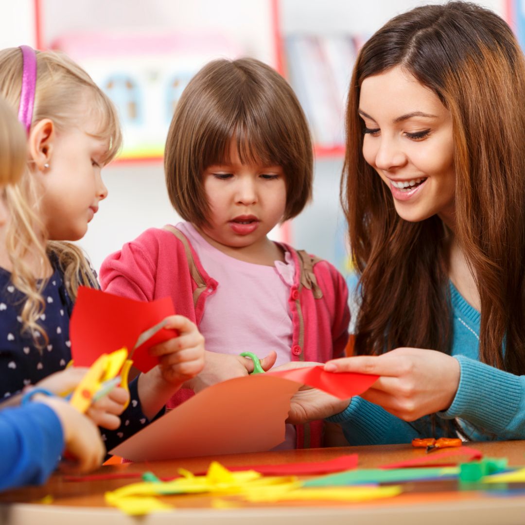 Daycare teacher helping children cut paper