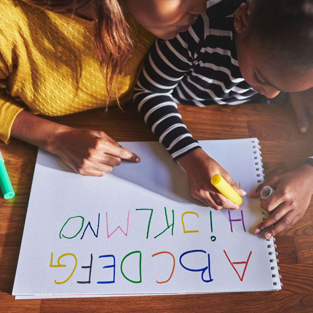 Child writing the alphabet on a notepad with markers 
