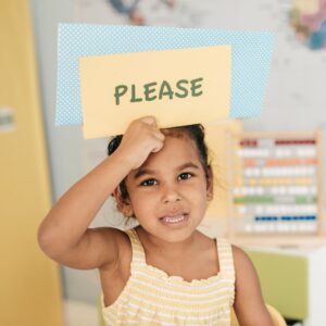Girl holding up a sign that says "please."