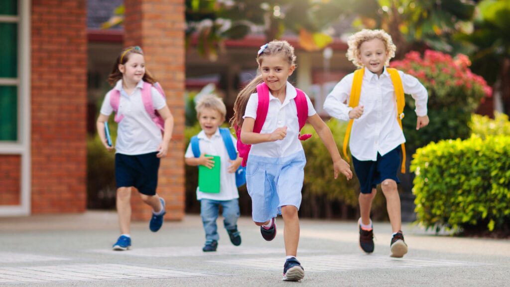 Four children running with backpacks on.